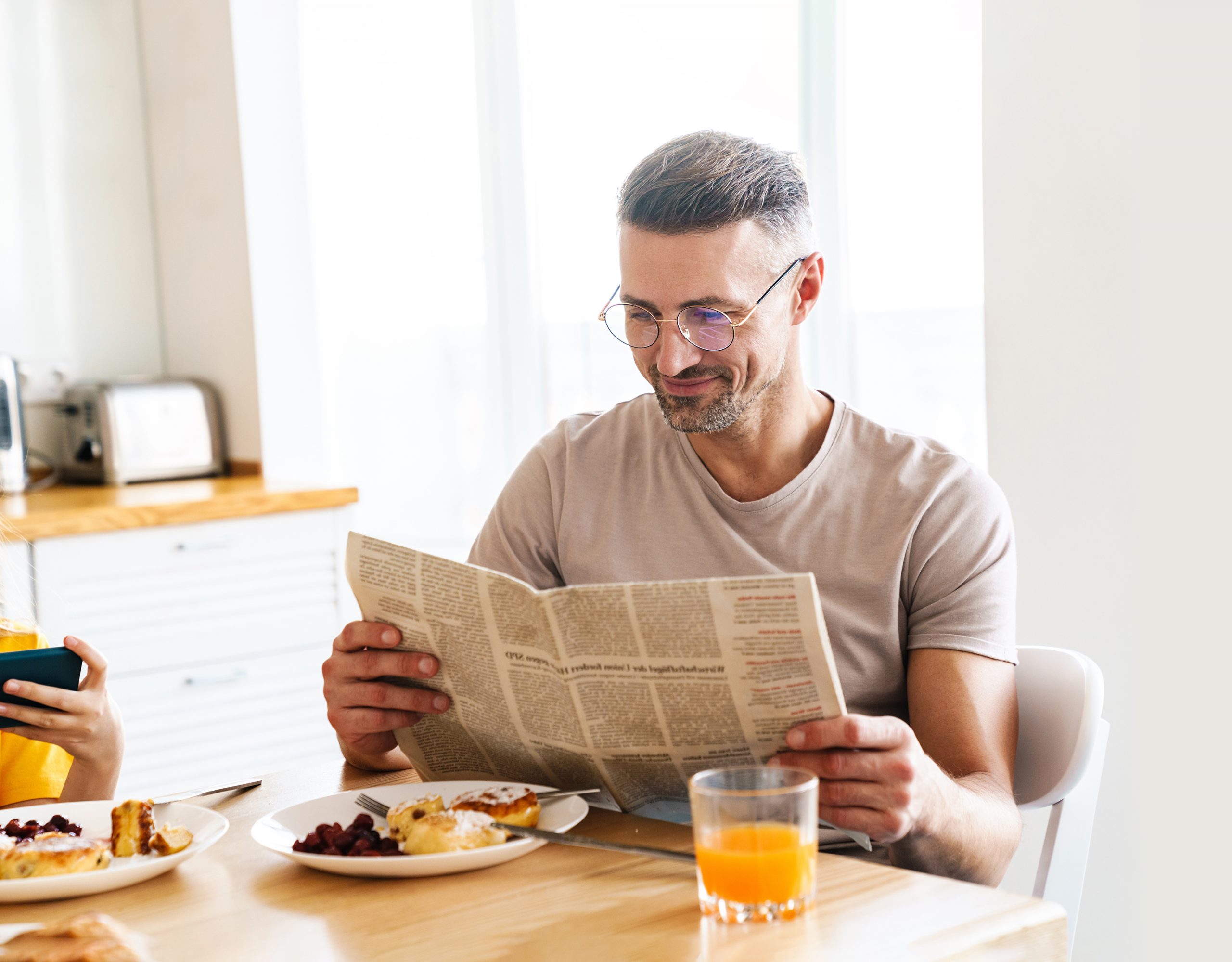 Photo of man reading newspaper while having breakfast